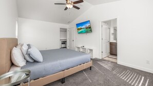 A bedroom with a bed, a ceiling fan, a TV, and a view of the kitchen.