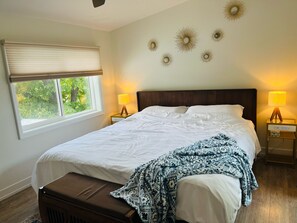 Una cama bien hecha con un edredón estampado, dos lámparas de noche, una ventana con persianas y decoración en la pared.