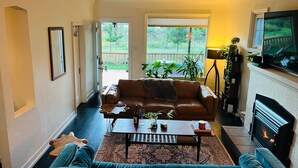 Sala de estar con sofá, mesa de centro, chimenea, televisor y vistas al exterior.