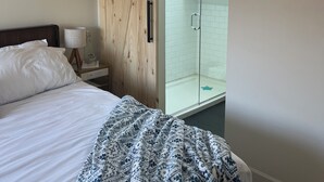 Un dormitorio con cama, armario de madera, ducha de vidrio y un gancho en la pared.