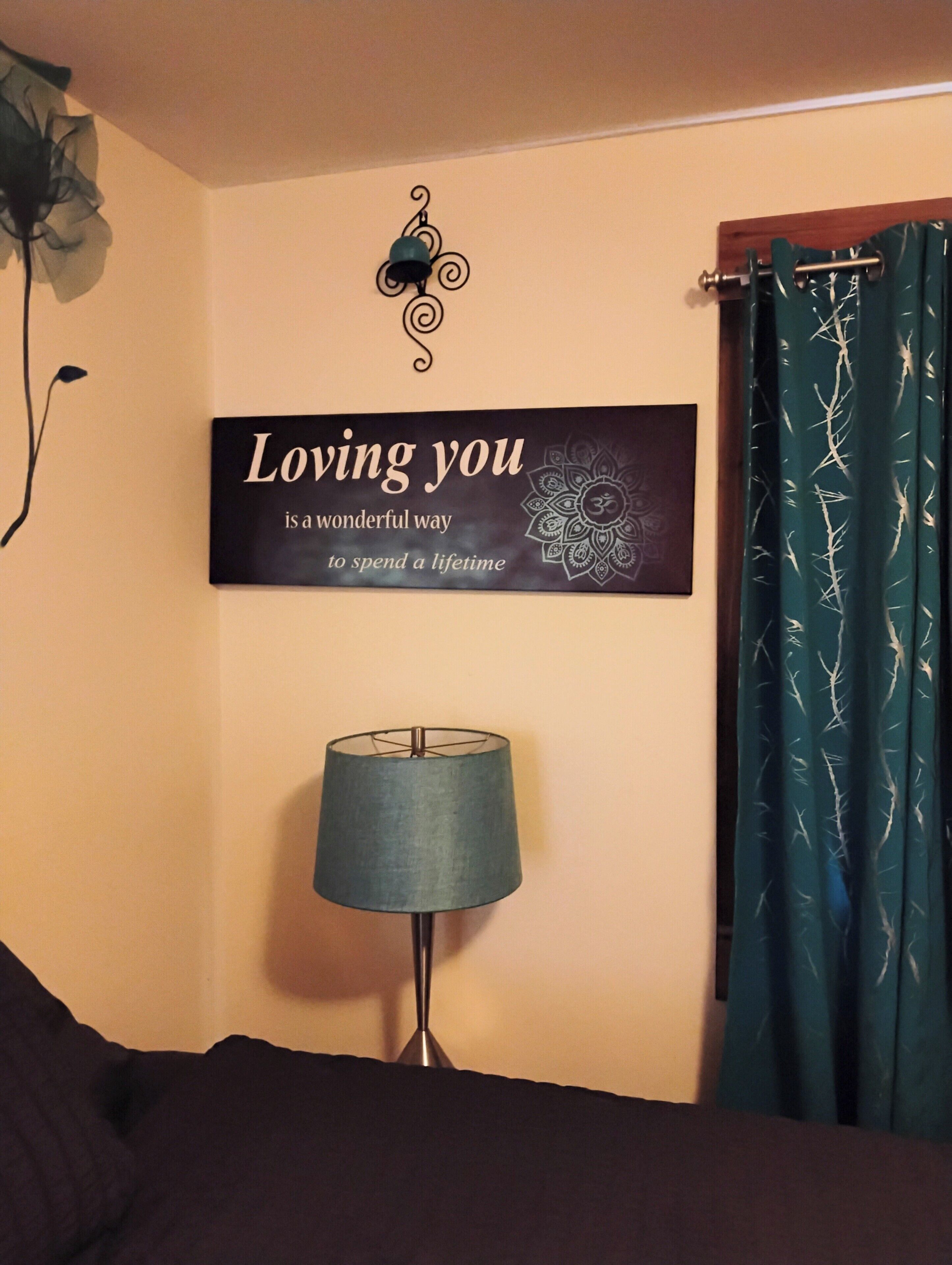 A bedroom with a bed, a wall-mounted sign, a lamp, and a curtain.