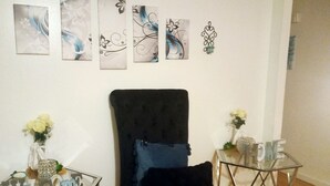 A room with a black upholstered chair, a glass table with 'Welcome' sign, and four framed artworks on the wall. - Charming -Clean-4-bedroom house with AC and WiFi in wonderful Springfield (Springfield)