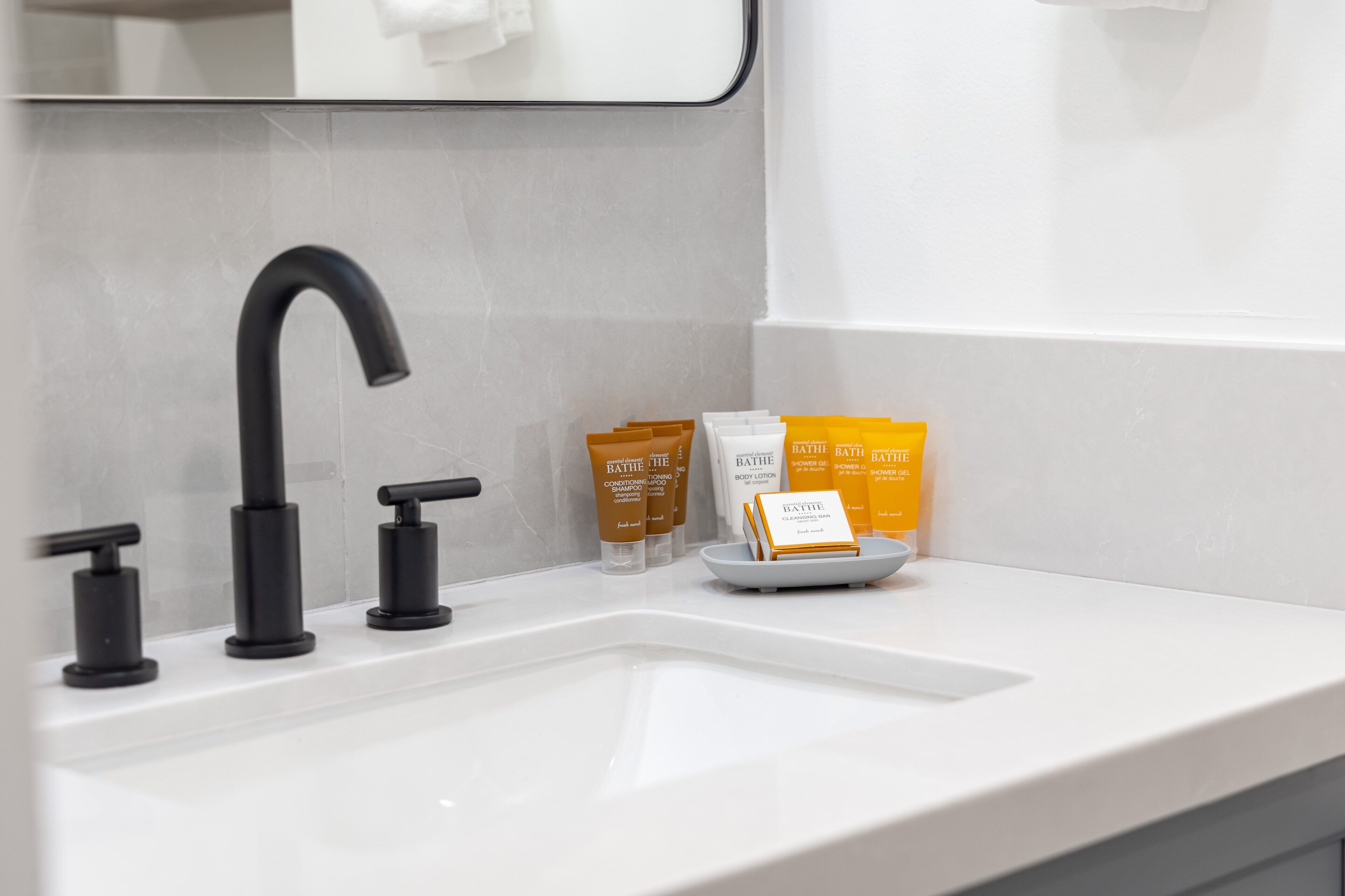 A bathroom with a white sink, black faucet, and toiletries including bath products.