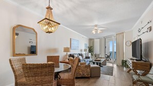 A spacious living room with a chandelier, a ceiling fan, a large mirror, and a television. - Palacio 803 (Pensacola)