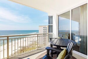 A balcony with a view of the ocean and beach, a table with chairs, and a large window with curtains. - Palacio 803 (Pensacola)