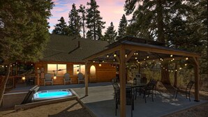 A wooden cabin with a hot tub, outdoor seating, and string lights. - Hidden Pines - Hot Tub, BBQ & Pool Table (Big Bear Lake)