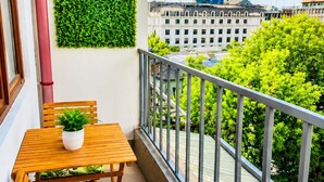 Ein Balkon mit Holztisch und -stühlen, einem Blumentopf und einer grünen Wand.