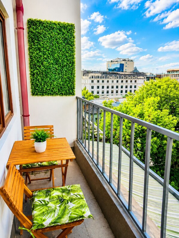 A balcony with a wooden table and chairs, a potted plant, and a green wall. - Old Town Ateneu Studio (Bucharest)