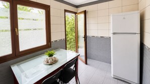 Eine Küche mit Kühlschrank, einem Esstisch mit Stühlen und einem Fenster mit Blick ins Grüne.