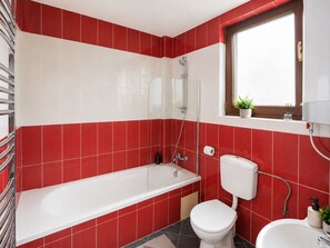 A bathroom with red and white tiles, a white bathtub, a toilet, and a window with a plant. - Old Town Ateneu Studio (Bucharest)