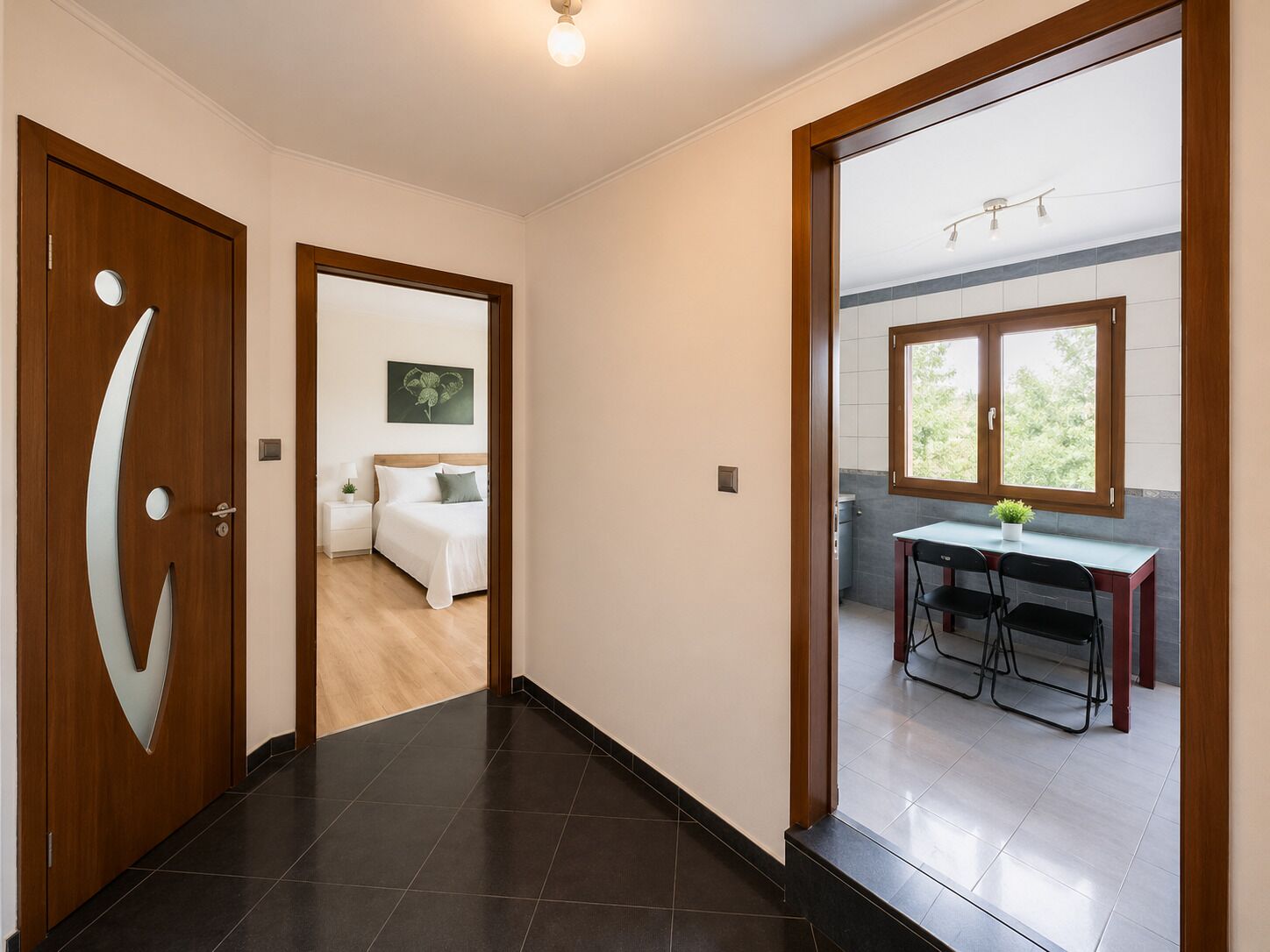A hallway leading to a bedroom with a bed, bedside table, and a wall-mounted artwork.