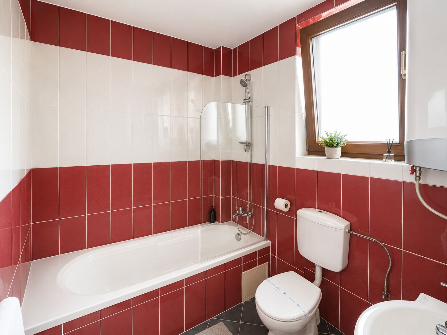 A bathroom with a bathtub, toilet, and sink, featuring red and white tiles.