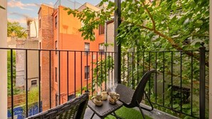 Een balkon met een tafel en stoelen, uitzicht op gebouwen en een metalen hek.