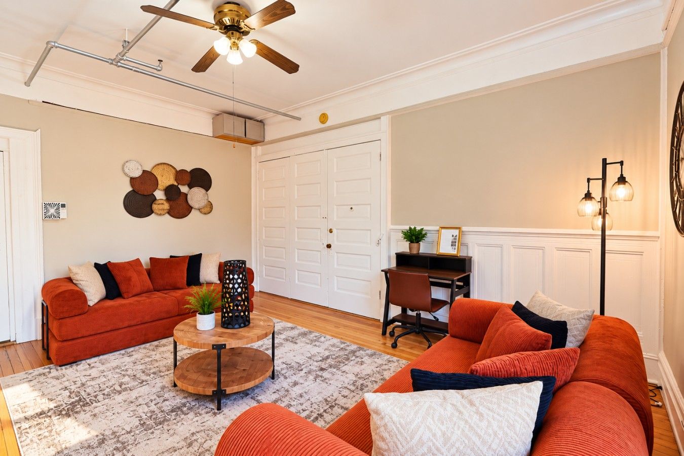 A living room with a sofa set, a coffee table, a desk, and a ceiling fan.
