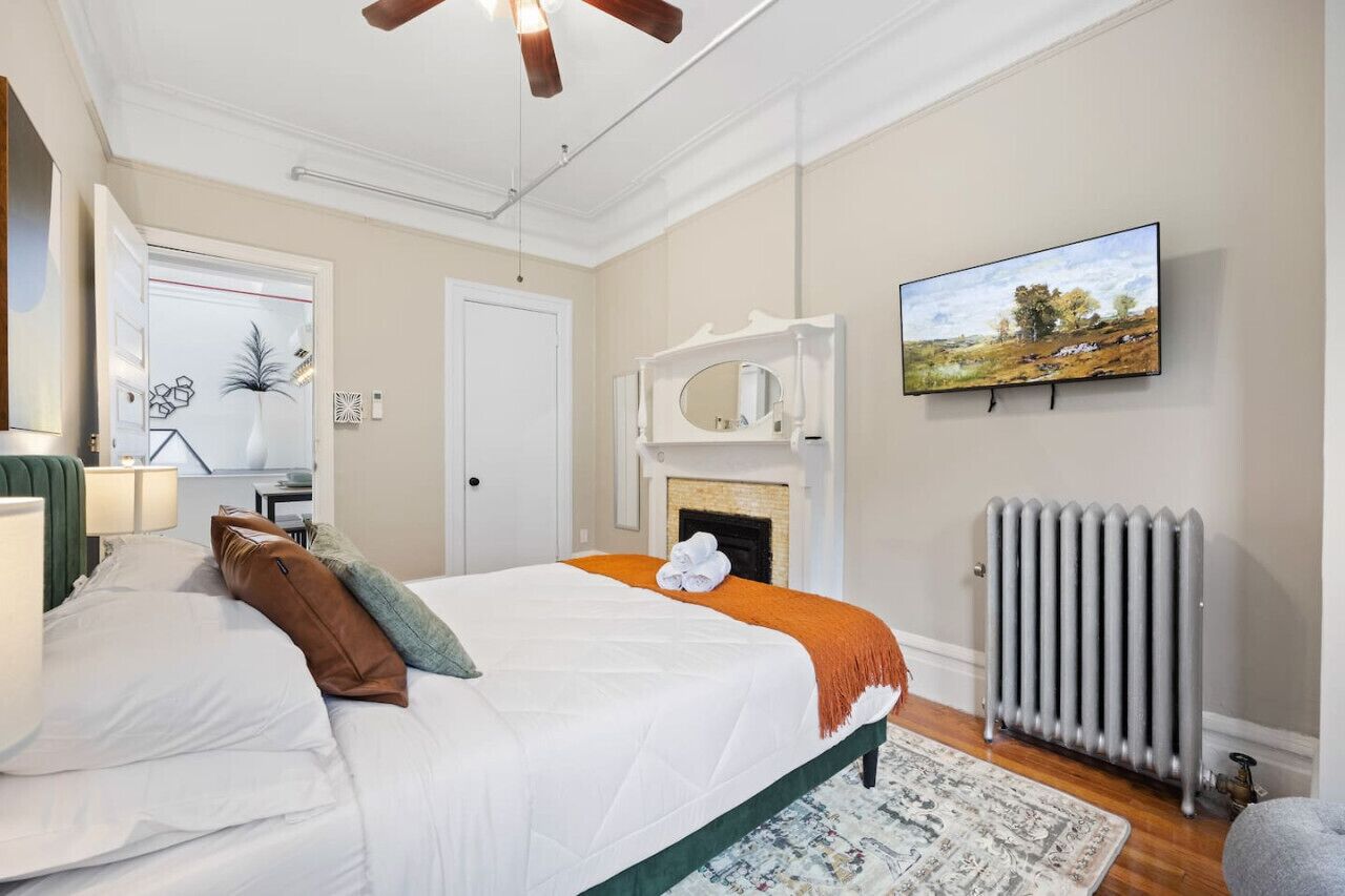 A bedroom with a bed, a fireplace, a radiator, and a television on the wall.