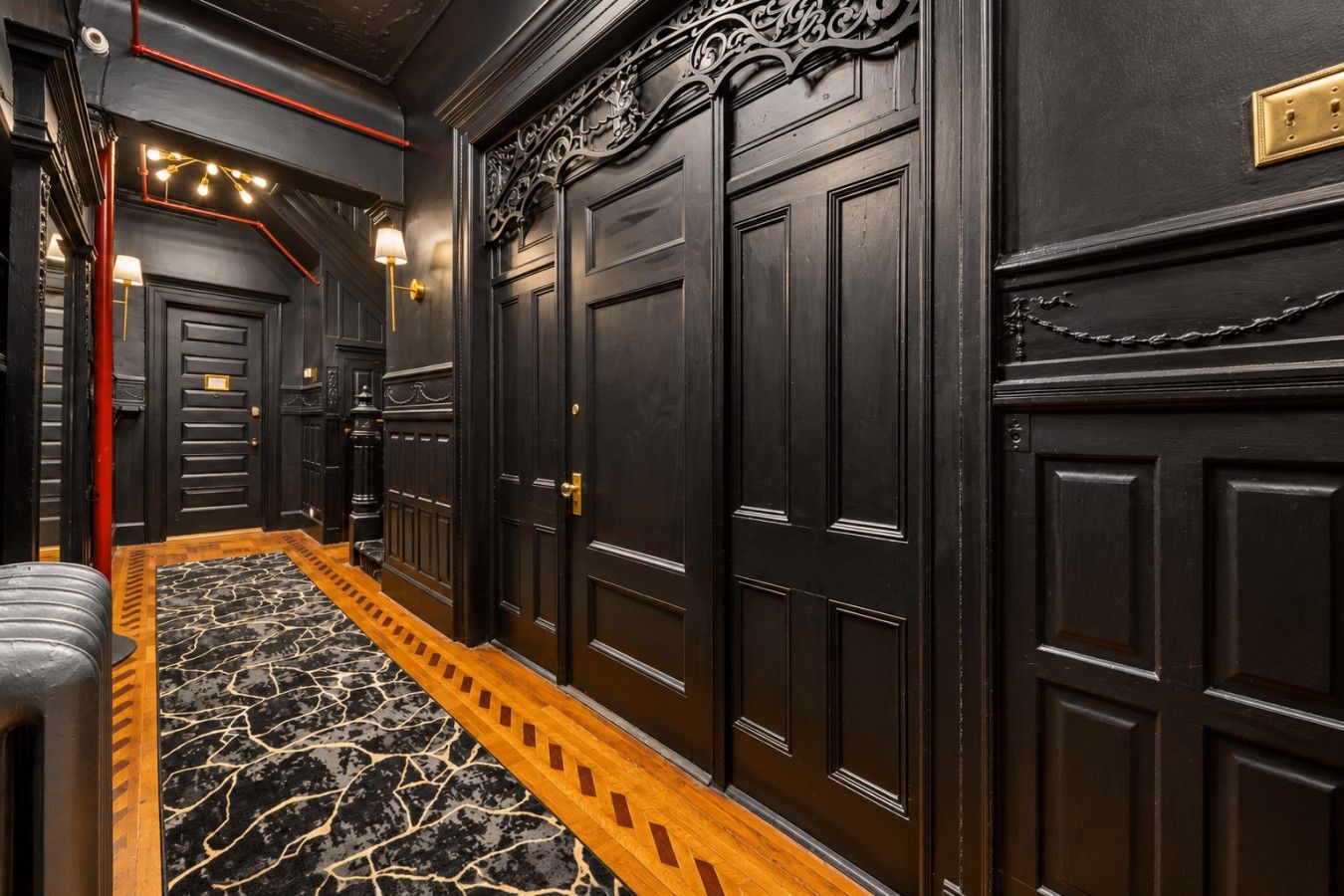 A hallway with dark wooden doors, a marble-patterned floor, and a red pipe running along the ceiling.