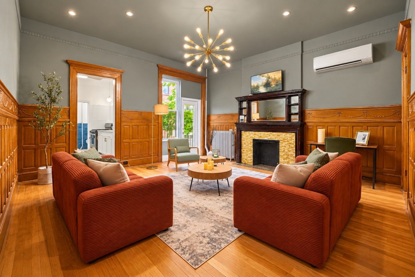 A spacious living room with a fireplace, two red sofas, a coffee table, and a modern chandelier.