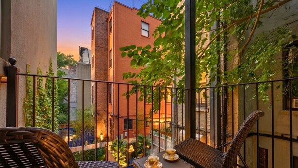 Ein Balkon mit Korbmöbeln, zwei Tassen auf einem Tisch und Blick auf Gebäude und Bäume.