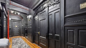 Ein Korridor mit dunklen Holztüren, einem fußbodenartig marmorierten Boden und einer roten Leitung, die an der Decke verläuft.