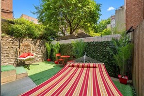 Um quintal com uma rede, um tapete de exterior riscado e vasos com plantas.