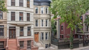 Una hilera de edificios de varios pisos con estilos arquitectónicos diversos, incluyendo un edificio en esquina con un ventanal semicircular y un árbol frente a él.