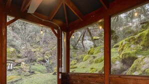 A wooden cabin with a bench and stone flooring, large windows offering a view of a forested landscape.