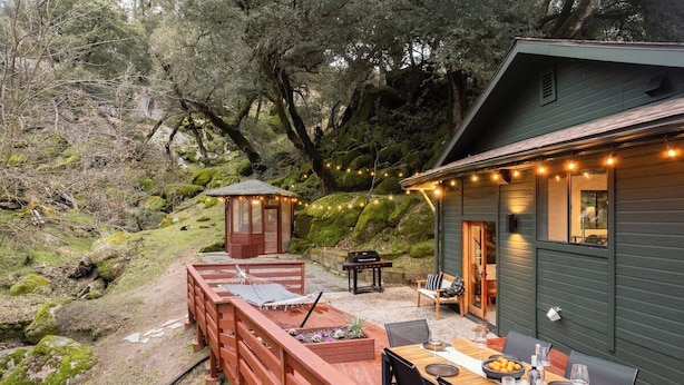 A wooden deck with a dining table and chairs, a small gazebo, and a house with string lights.