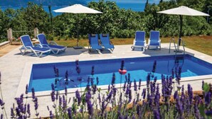 En swimmingpool med blått vatten, omgiven av solstolar och parasoller, med utsikt över berg och grönskande landskap i bakgrunden.
