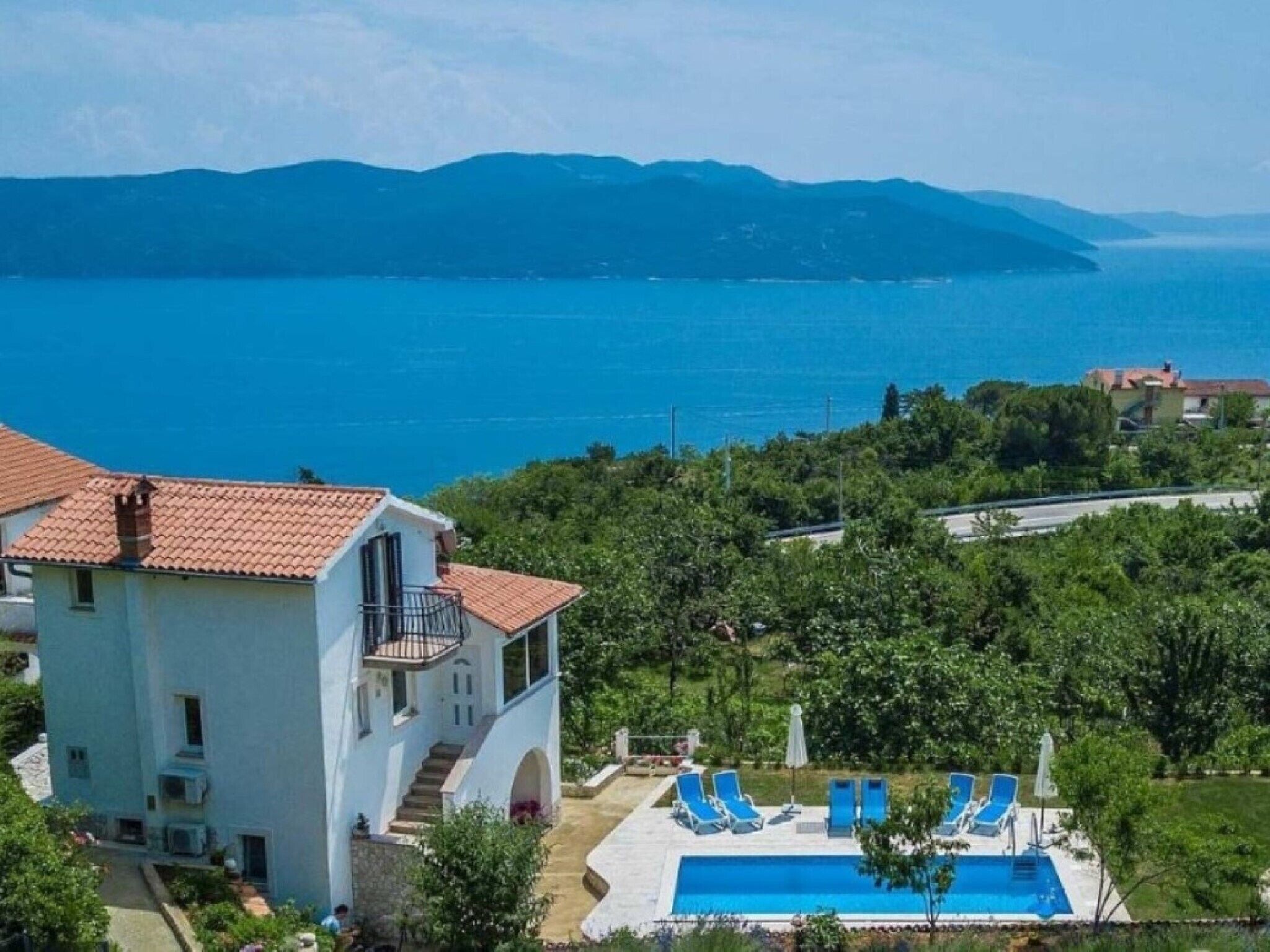 A coastal property with a swimming pool, lounge chairs, and a view of the sea and mountains.