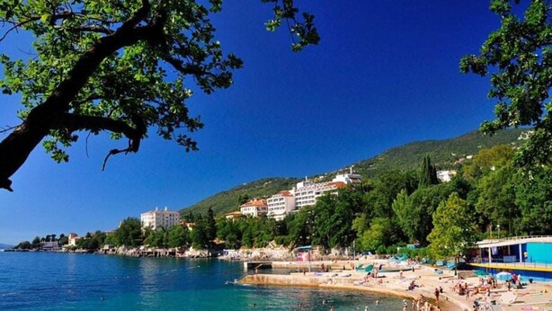 A coastal area with a beach, people swimming, and buildings on a hillside.