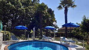 A swimming pool with lounge chairs and umbrellas, surrounded by trees and a clear sky.
