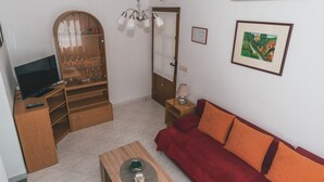 A living room with a TV, wooden furniture, a red sofa, a glass cabinet with wine glasses, and a painting on the wall.