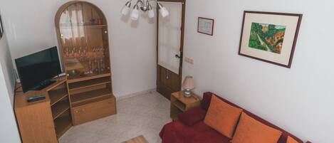 A living room with a TV, wooden furniture, a red sofa, a glass cabinet with wine glasses, and a painting on the wall.