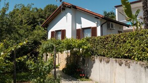 A white house with a red roof, surrounded by greenery and a stone wall.