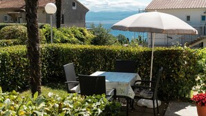 An outdoor seating area with a table and chairs, surrounded by greenery and a view of the sea.