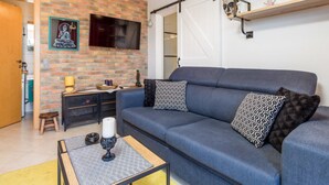 A living room with a blue sofa, patterned cushions, a coffee table, and a brick wall with a mounted TV.