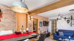 A modern living space with a dining area, a blue sofa, and a TV mounted on the wall.