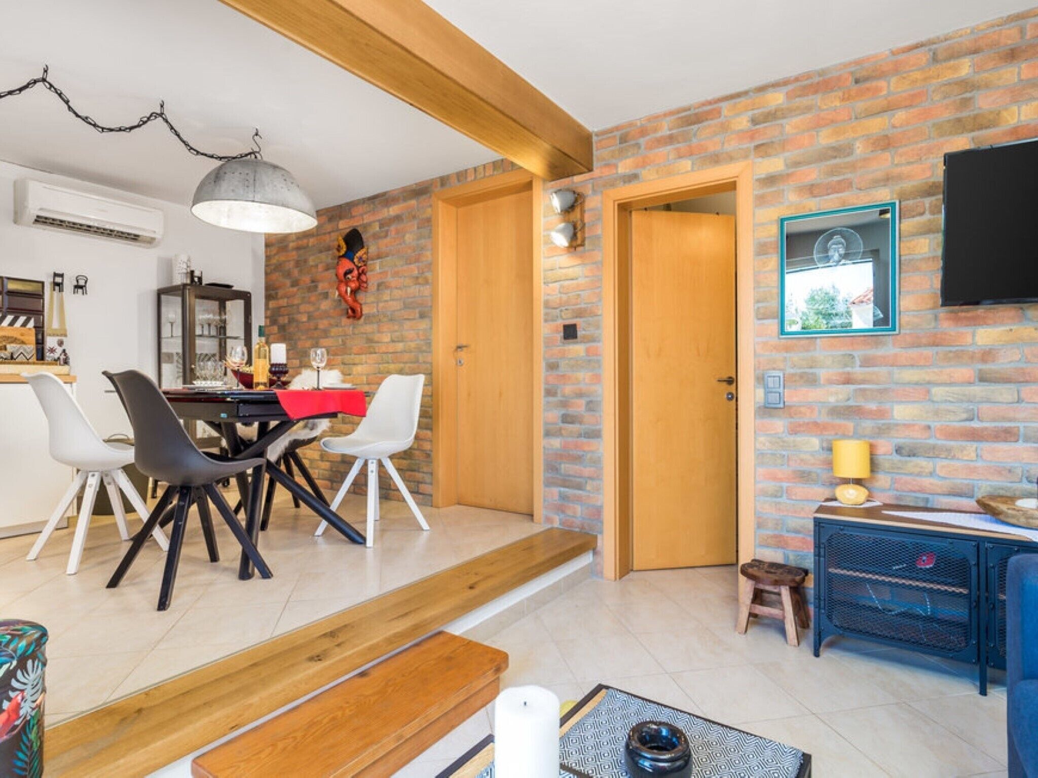 A dining area with a brick wall, a wooden door, and a TV mounted on the wall.