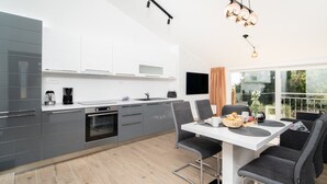 Moderni keittiö, jossa on harmaat kaapit, sisäänrakennettu uuni sekä ruokailutila, jossa on pöytä ja tuolit.