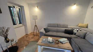 A modern living room with a grey sofa, a wooden coffee table, a floor lamp, and a glass table with a vase.