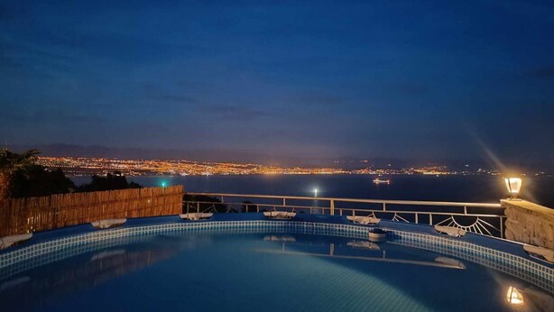 Ein Blick auf ein Schwimmbecken bei Nacht, im Hintergrund die Skyline einer Stadt.