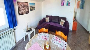 Une petite pièce accueillante, avec un canapé violet, une petite table recouverte d’une nappe à motifs floraux et un radiateur.