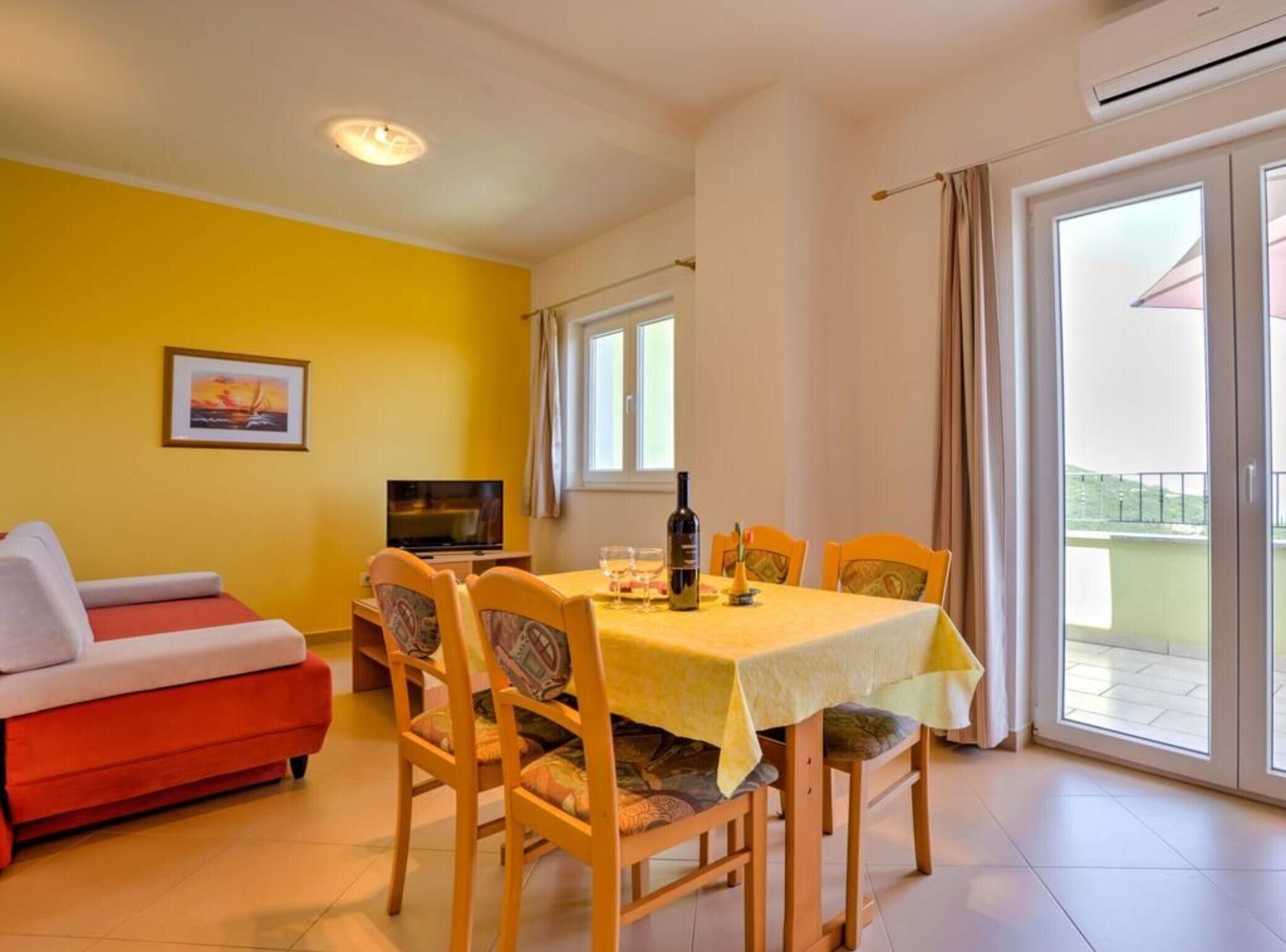 Un comedor con una mesa preparada para cuatro, un sofá, un televisor y un cuadro en la pared.