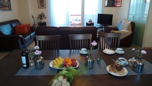 Un coin repas avec une table mise pour le repas, des chaises, un canapé, un téléviseur et une fenêtre avec des rideaux.