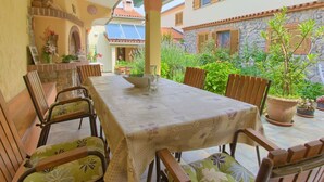 Un espace de restauration en plein air, avec une table et des chaises, entouré de plantes en pot et d’un mur en pierre.