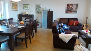Un salon avec un canapé marron foncé, une table à manger dressée avec des assiettes et des verres, et une guitare posée dans un coin.