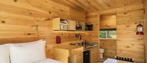 Una cabaña de madera compacta con kitchenette, una cama y un baño pequeño.