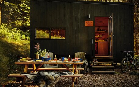 A cabin with a dining table set outdoors, a bicycle, and a sign indicating the name 'Vangelis'.