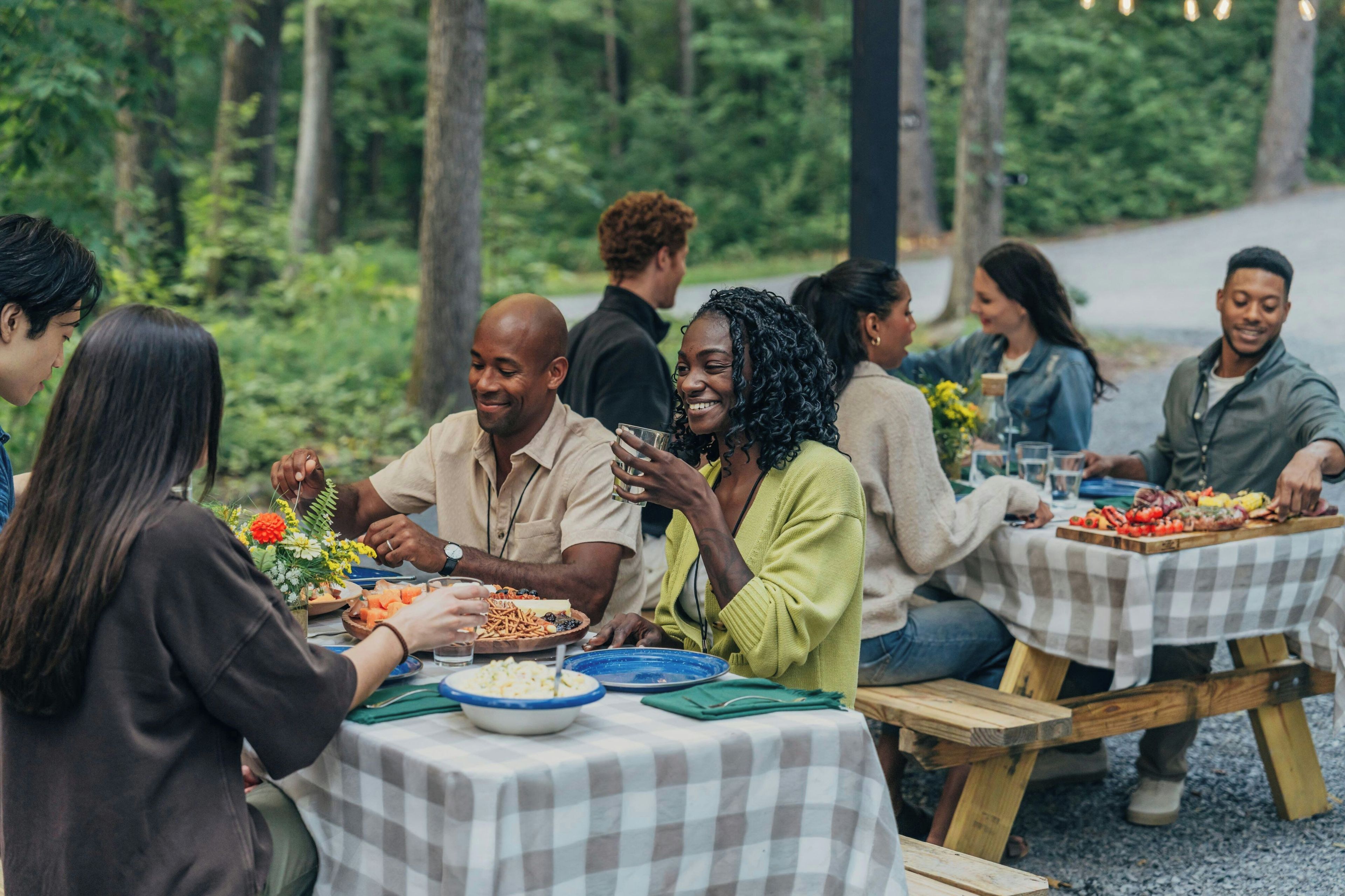 A group of people dining outdoors at a picnic table with a checkered tablecloth.