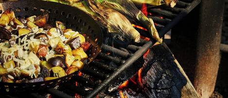 Una parrilla con verduras y mazorcas de maíz asándose al fuego.